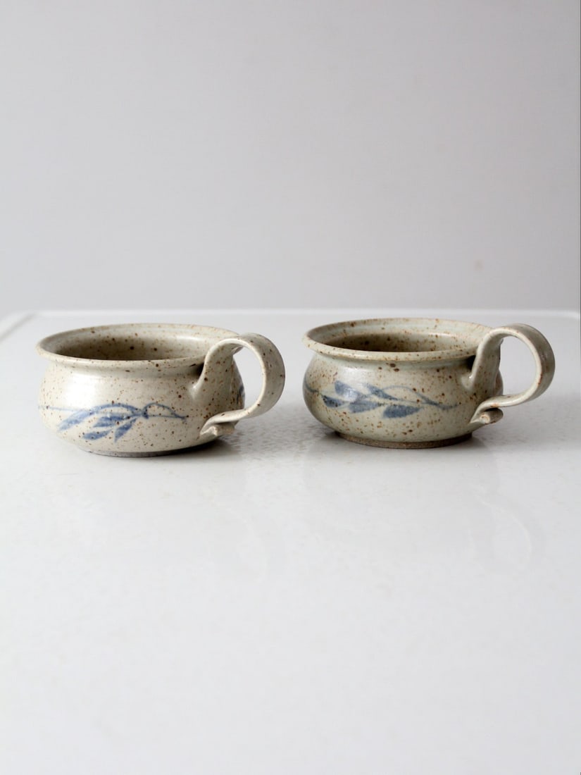 Vintage Studio Pottery Soup Mugs Pair with Floral Motifs: Vintage Studio Pottery Soup Mugs Pair with Floral Motifs This charming pair of vintage studio pottery soup mugs showcases a speckled cream glaze complemented by delicate blue floral motifs. The handcr