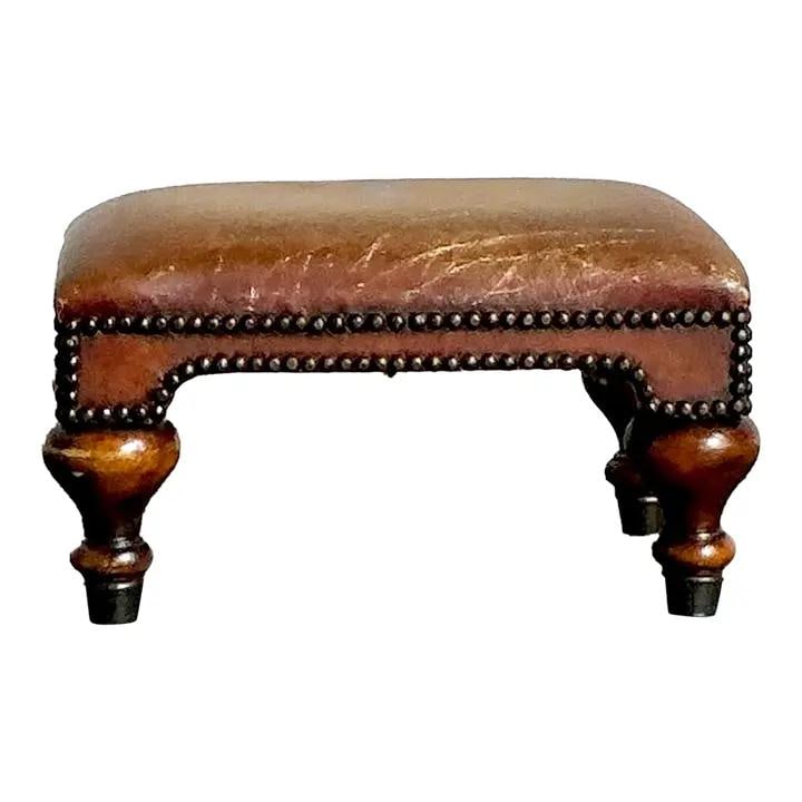 Embossed Leather Footstool With Royal Crest and Turned Wood Feet: Embossed Leather Footstool With Royal Crest and Turned Wood Feet This vintage leather footstool features a rectangular cushion upholstered in cognac-brown leather embossed with a faded royal coat of