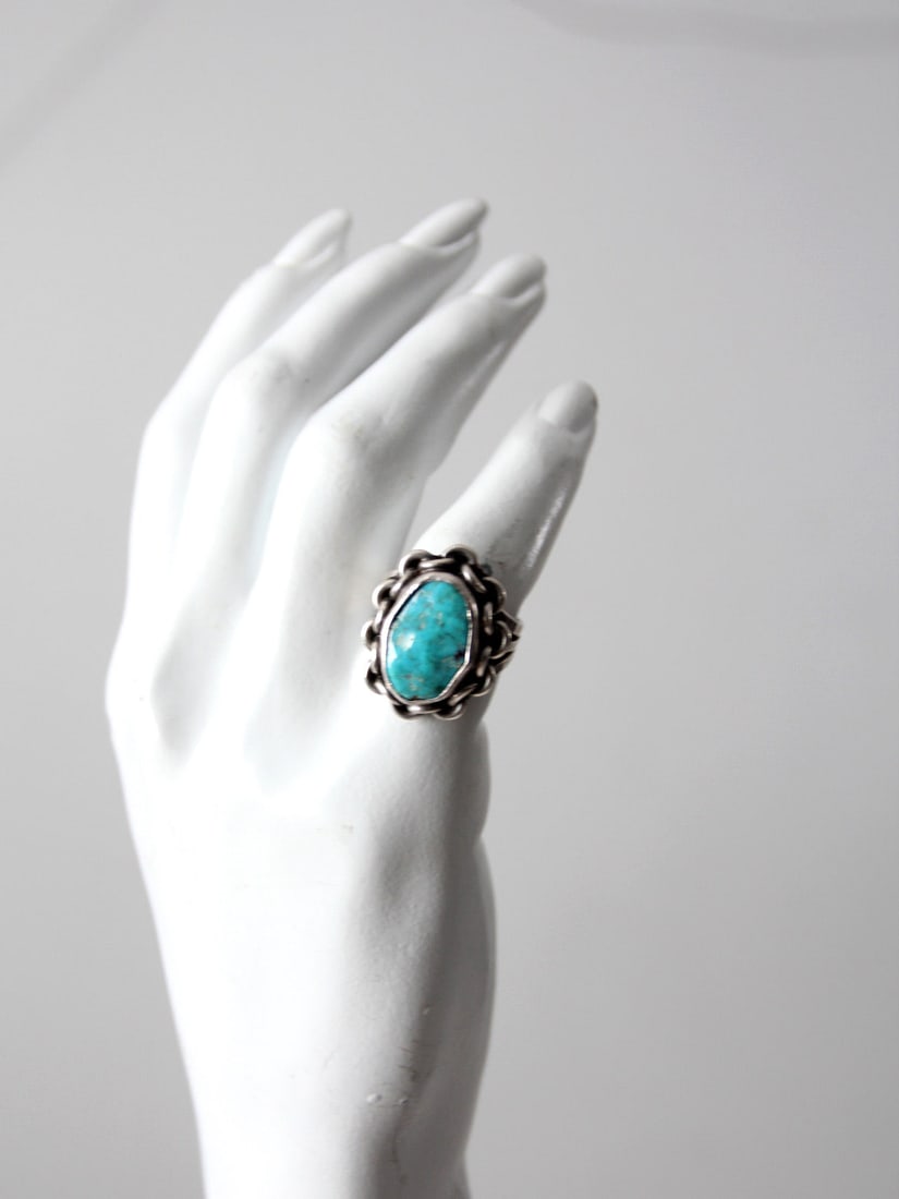 1970s Turquoise Statement Ring Silver Tone Size 6.5: 1970s Turquoise Statement Ring Silver Tone Size 6.5 This vintage 1970s turquoise ring features a vivid blue stone set in a sculptural metal setting with a distinctive chain-like border. The softened f