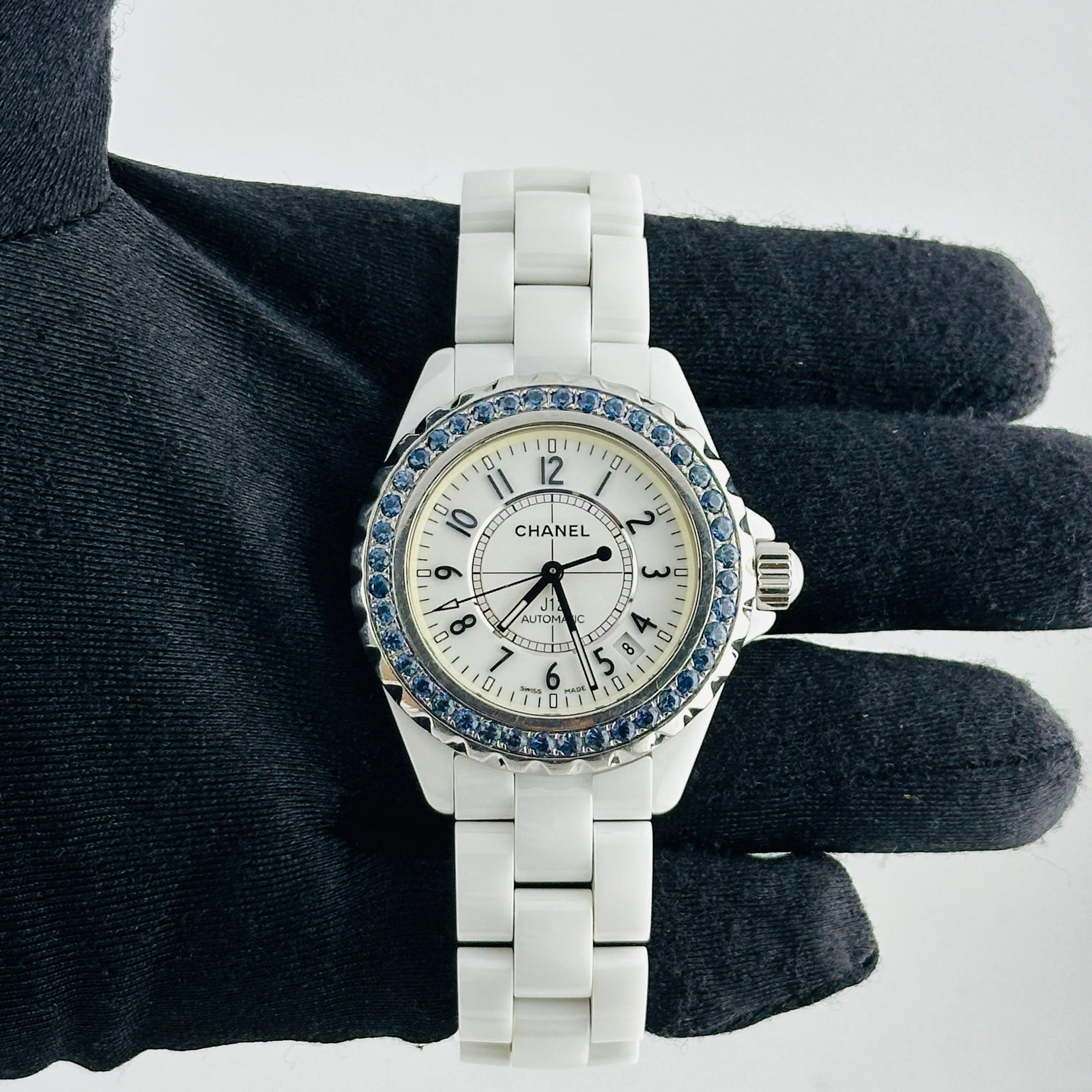 Chanel J12 Ceramic Bracelet White Arabic Dial Ref H1179: Chanel J12 Ceramic Bracelet White Arabic Dial Ref H1179 This Chanel J12 watch features a white dial with Arabic numerals and is paired with a ceramic bracelet. The bezel is set with factory blue diamo