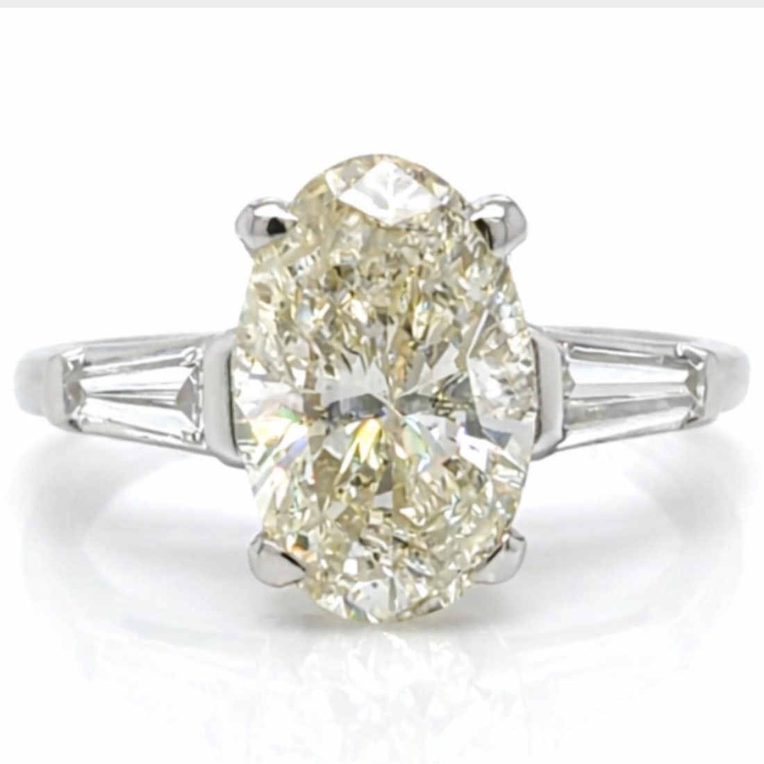2.39 Carat Oval Diamond Platinum Engagement Ring with Baguette Accents 1950s: 2.39 Carat Oval Diamond Platinum Engagement Ring with Baguette Accents 1950s This 1950s platinum engagement ring features a 2.39 carat oval diamond with M color and I2 clarity as its centerpiece. It i