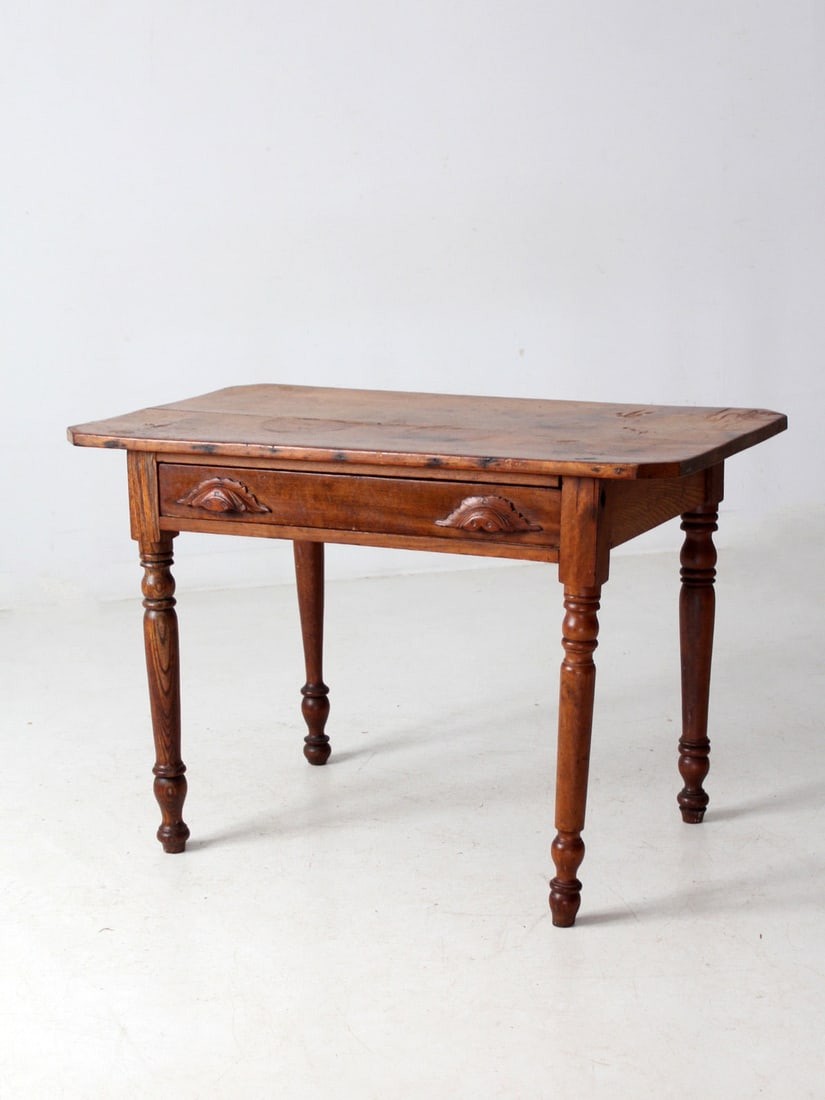 Rustic Antique Primitive Table with Drawer and Turned Legs: Rustic Antique Primitive Table with Drawer and Turned Legs This antique primitive table showcases the charm of aged wood with its richly patinated plank top and naturally timeworn surface. It features