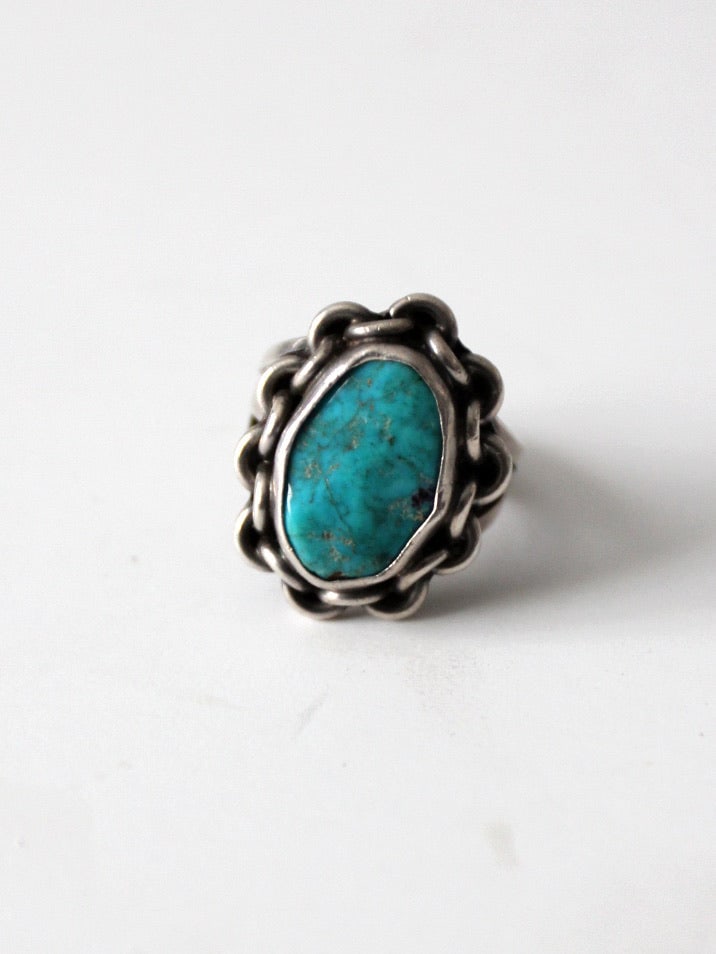 1970s Turquoise Statement Ring Silver Tone Size 6.5: 1970s Turquoise Statement Ring Silver Tone Size 6.5 This vintage 1970s turquoise ring features a vivid blue stone set in a sculptural metal setting with a distinctive chain-like border. The softened f