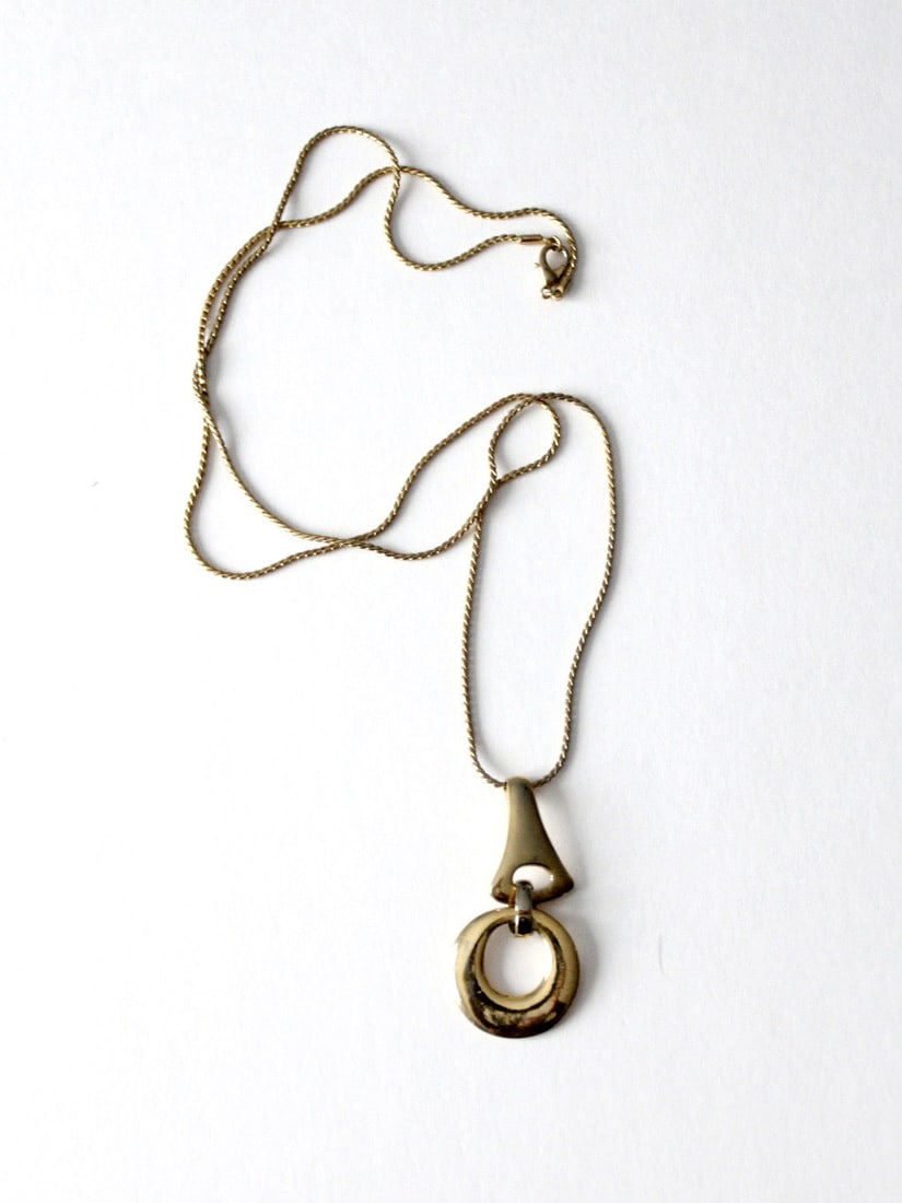 Modernist Gold Tone Necklace With Sculptural Geometric Drop Pendant 34 Inch Chain: Modernist Gold Tone Necklace With Sculptural Geometric Drop Pendant 34 Inch Chain This vintage pendant necklace features a sculptural drop with fluid curves and geometric elements, suspended from a sl