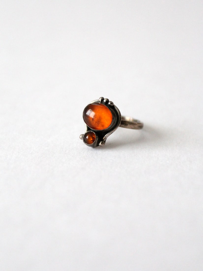Vintage Silver Tone Ring with Amber Stone Settings: Vintage Silver Tone Ring with Amber Stone Settings This vintage statement ring features a silver tone design adorned with two beautiful orange stone settings, believed to be amber. The ring is in good