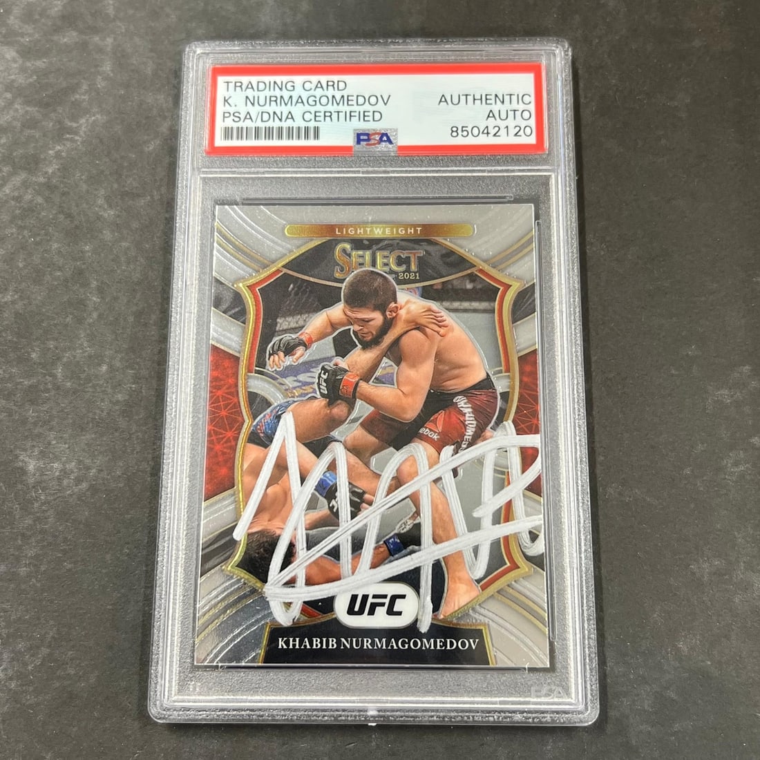 2021 Panini Select UFC Khabib Nurmagomedov Signed Card PSA Authenticated: 2021 Panini Select UFC Khabib Nurmagomedov Signed Card PSA Authenticated This is a 2021 Panini Select #47 trading card featuring the renowned fighter Khabib Nurmagomedov. The card showcases his autogr