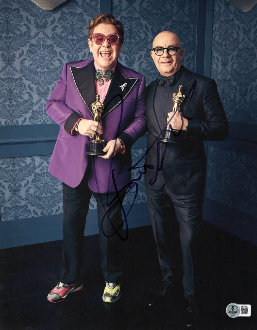 Bernie Taupin Signed 11x14 Photo with Elton John BAS Authentication: Bernie Taupin Signed 11x14 Photo with Elton John BAS Authentication This striking 11X14 photograph features Bernie Taupin, famously known as Elton John's longtime collaborator, holding awards. The ima