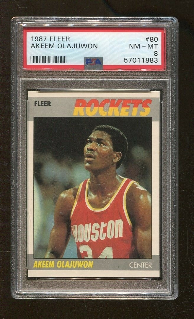 Akeem Olajuwon 1987 Fleer Rockets Trading Card PSA 8: Akeem Olajuwon 1987 Fleer Rockets Trading Card PSA 8 This original 1987 Fleer basketball card features the legendary player Akeem Olajuwon, known for his remarkable skills on the court. Graded PSA 8, 