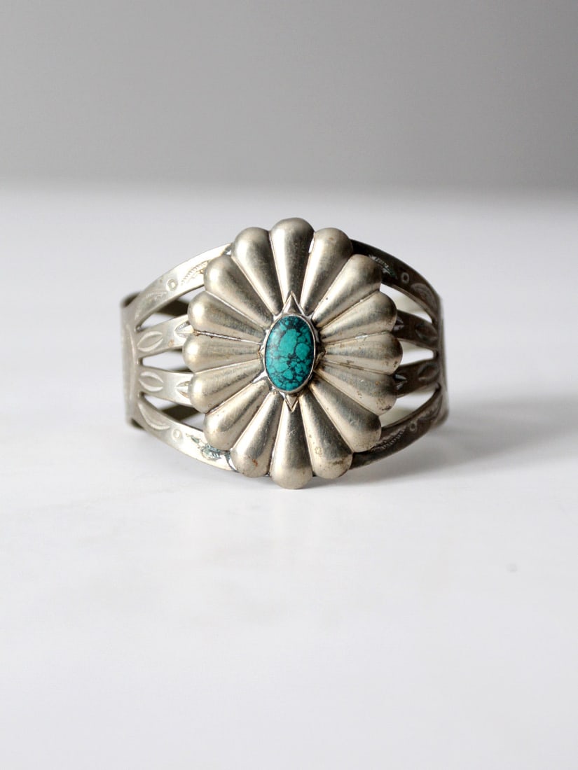Southwestern Silver Tone Cuff Bracelet with Turquoise Stone Accent: Southwestern Silver Tone Cuff Bracelet with Turquoise Stone Accent This vintage cuff bracelet features a turquoise stone at its center, set within a sculptural, radiating design. The wide band showcas