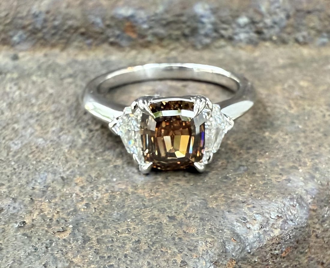 GIA Platinum Cocktail Ring Fancy Orangy Brown Diamond Trio: GIA Platinum Cocktail Ring Fancy Orangy Brown Diamond Trio This un-used platinum cocktail ring features a unique three-stone design highlighted by a GIA-certified, natural step cut diamond at its cent