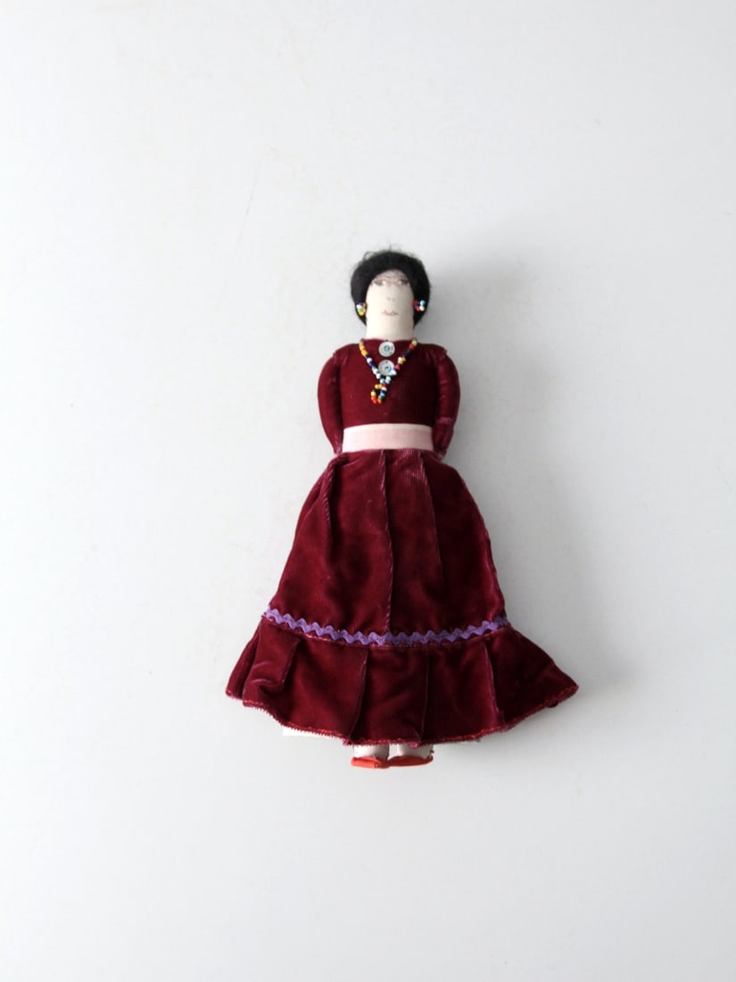 Navajo Vintage Doll with Beaded Jewelry and Floral Clothing: Navajo Vintage Doll with Beaded Jewelry and Floral Clothing This vintage Native American doll showcases the artistry of the Navajo culture. Featuring a painted cloth face, the doll is adorned with dec