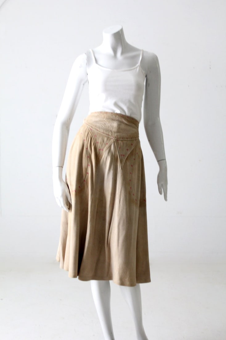 Cisco beige suede wrap skirt with pink accents and pockets: Cisco beige suede wrap skirt with pink accents and pockets This vintage suede wrap skirt features soft beige leather accented with pink square details at the waist and pockets. Designed with two pocke