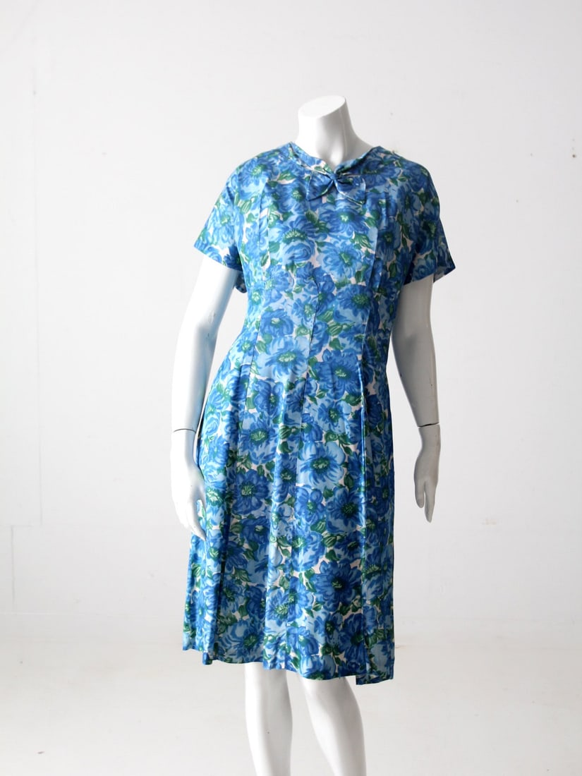 Charming 1950s Floral Print Dress with Bow Neckline: Charming 1950s Floral Print Dress with Bow Neckline Step back in time with this charming vintage 1950s floral dress. Featuring a delightful blue and green floral pattern, this dress boasts a darted bu
