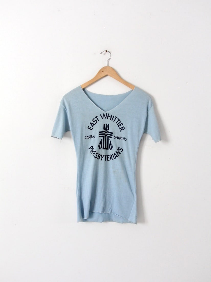1980s Vintage East Whittier Graphic Tee Soft Blue V-Neck: 1980s Vintage East Whittier Graphic Tee Soft Blue V-Neck Discover this authentic 1980s vintage graphic t-shirt featuring a soft blue color and a fitted v-neck design, showcasing the East Whittier Pres