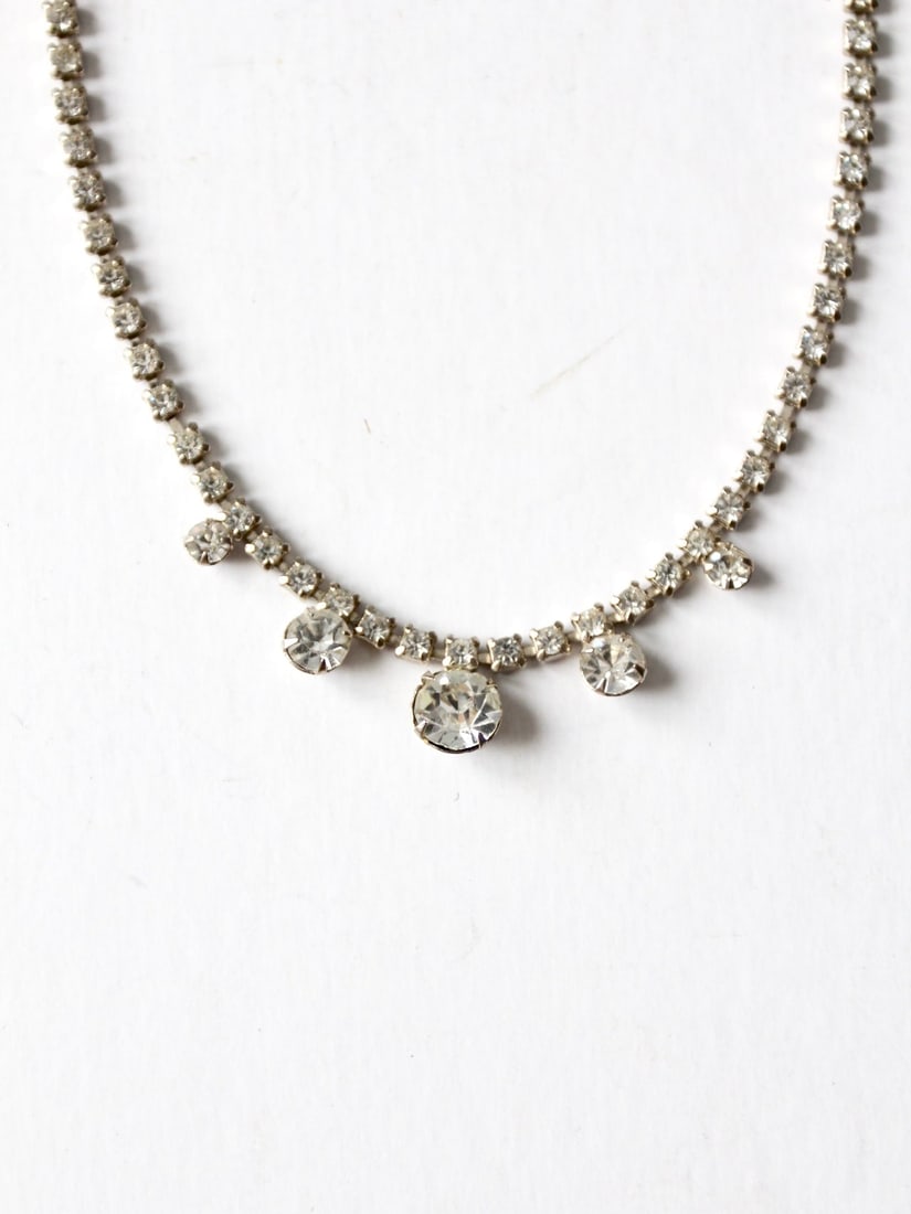 Prong Set Rhinestone Chain Necklace with Graduated Center Pendants: Prong Set Rhinestone Chain Necklace with Graduated Center Pendants This vintage rhinestone necklace features a prong-set rhinestone chain with graduated pendants at the center, offering a sparkling an