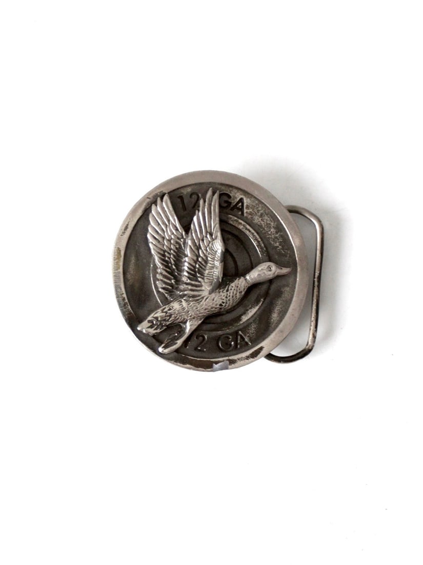 1980 Mallard Belt Buckle Silver Tone Cast Metal Made in USA: 1980 Mallard Belt Buckle Silver Tone Cast Metal Made in USA Vintage 1980 belt buckle with a duck hunting motif, featuring a flying mallard in raised relief over a 12 gauge shotgun shell. The silver-to