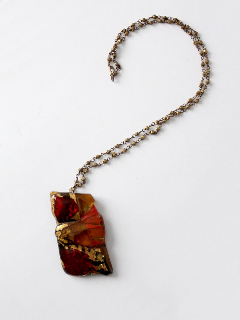Vintage 60s Resin Pendant Necklace Brass Chain Mod Style: Vintage 60s Resin Pendant Necklace Brass Chain Mod Style This vintage 60s pendant necklace features a striking large resin pendant with a vibrant swirl of rust red, orange, gold, and black colors. The