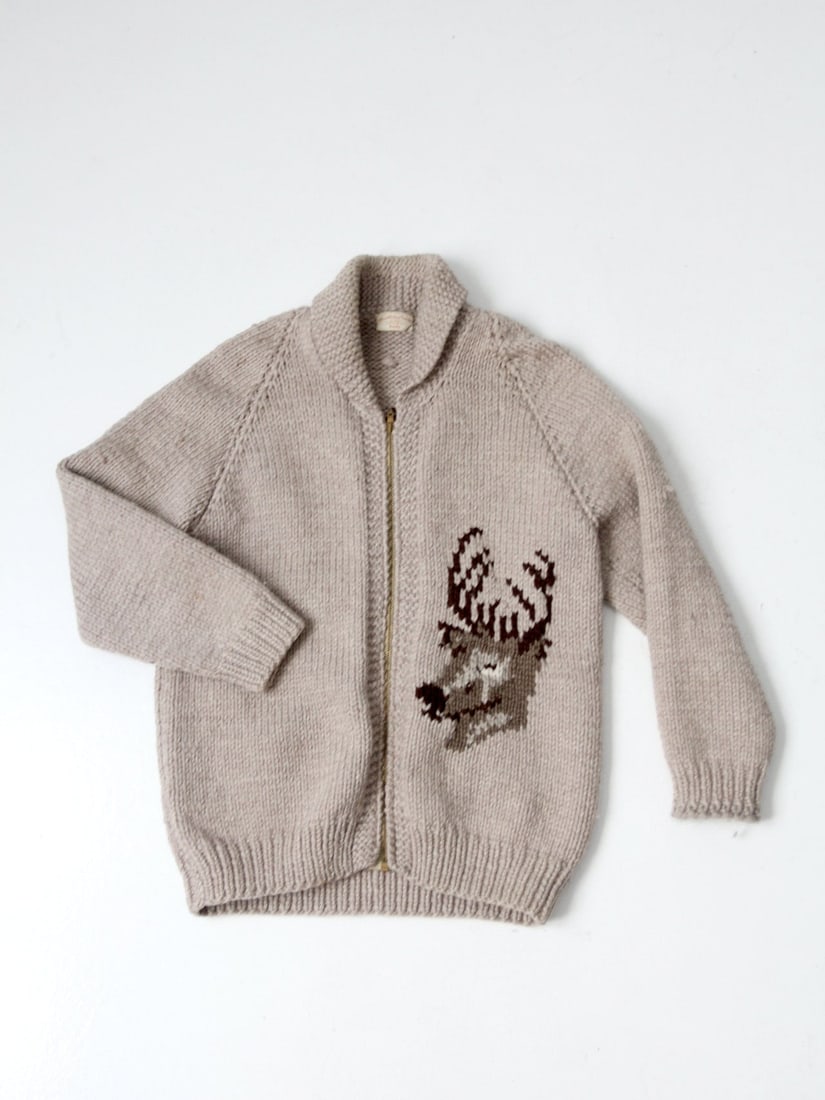 Vintage Hand Knit Tan Wool Camp Sweater with Deer Design: Vintage Hand Knit Tan Wool Camp Sweater with Deer Design Discover a unique vintage hand-knit camp sweater, crafted from thick tan wool. This cardigan features an eye-catching deer head design on the f