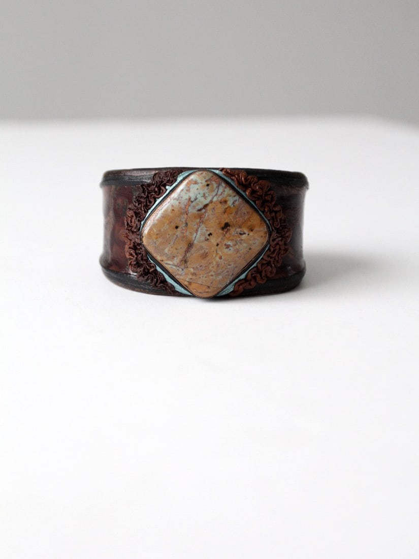 Vintage Leather Cuff with Turquoise Stone Detail: Vintage Leather Cuff with Turquoise Stone Detail Discover the unique charm of this vintage leather cuff, expertly crafted from dark brown leather and featuring a stunning inset stone. The centerpiece 