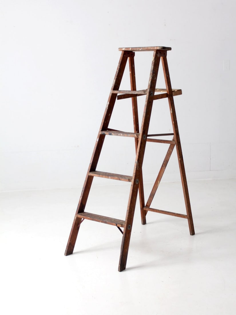 Vintage wooden A-frame painter ladder with shelf: Vintage wooden A-frame painter ladder with shelf This vintage wooden painter's ladder features an a-frame design with four rung steps, a back shelf, and a cross back brace. It has a warm tone and disp
