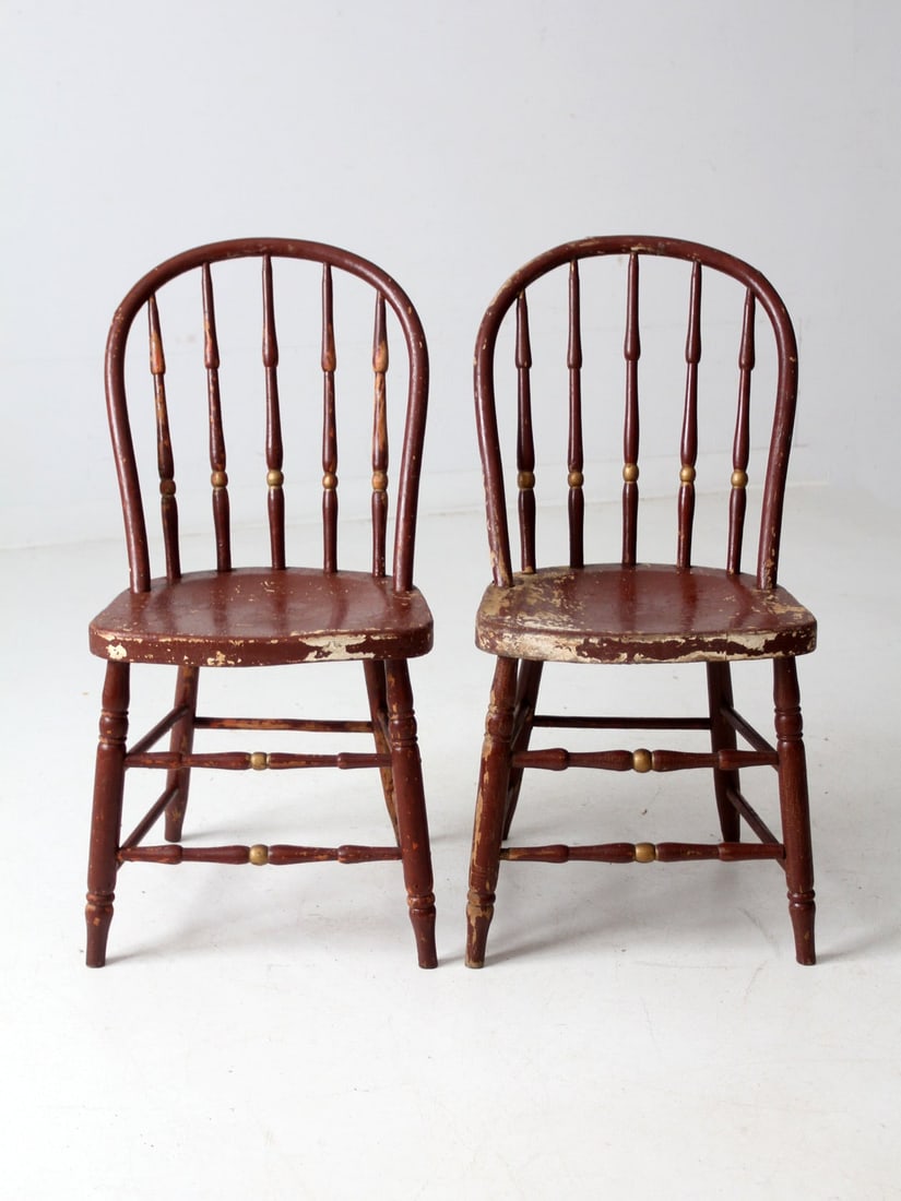 Vintage Pair of Antique Maroon Spindle Back Chairs: Vintage Pair of Antique Maroon Spindle Back Chairs This pair of antique Windsor-style spindle back chairs showcases a maroon painted finish with elegant gold accents, revealing areas of wear that cont