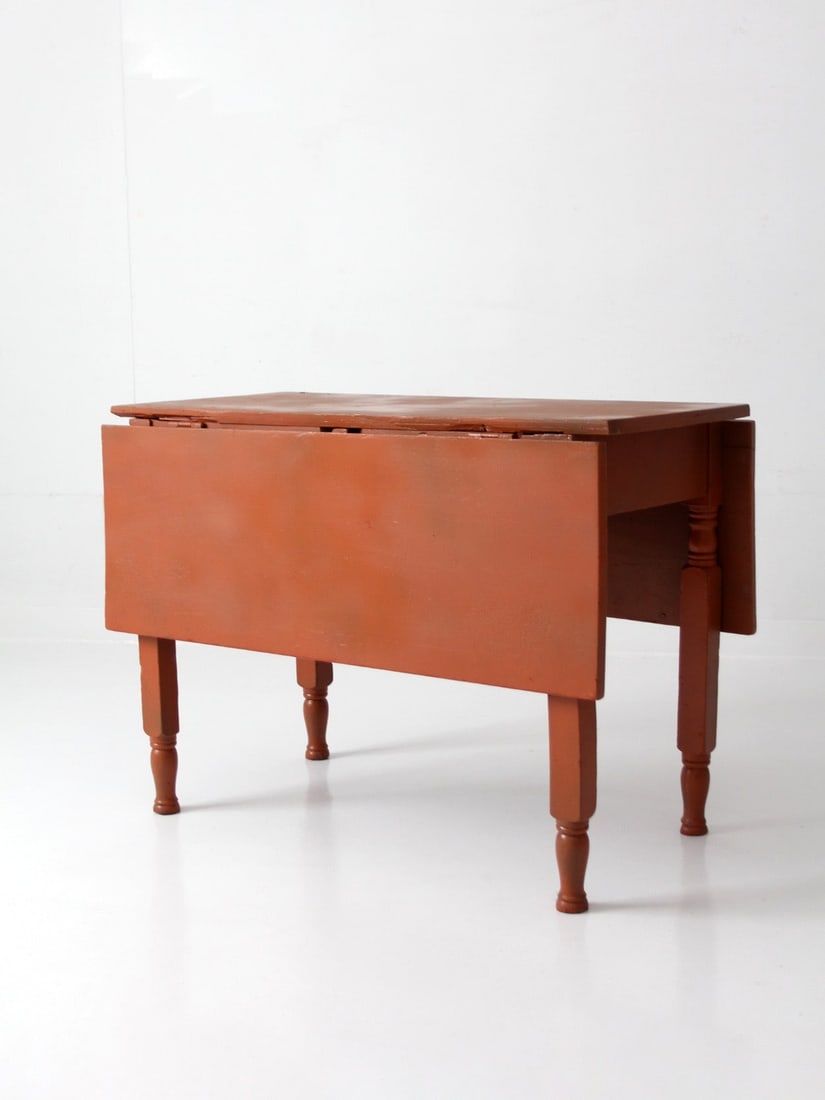 Early 20th Century Painted Drop Leaf Farmhouse Table: Early 20th Century Painted Drop Leaf Farmhouse Table This early 20th century drop leaf table features turned legs and a compact farmhouse design, making it ideal for smaller interiors. The hinged leav