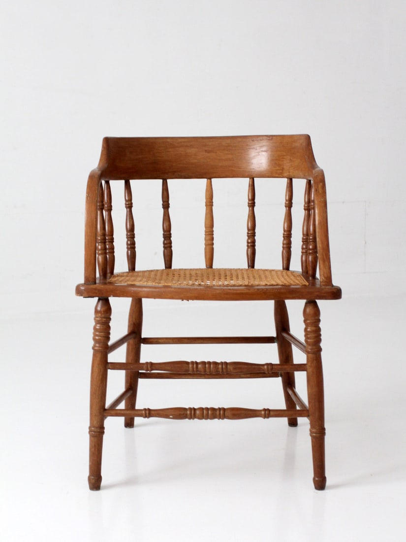 Colonial Revival cane seat captain chair with shaped arms: Colonial Revival cane seat captain chair with shaped arms This antique captain's chair features a hand-caned seat, a curved crest rail, and shaped arms supported by turned spindles. The chair's constr
