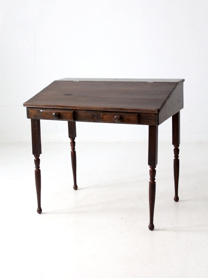 1940s Vintage Slant Top Wood Desk with Hinged Top and Turned Legs: 1940s Vintage Slant Top Wood Desk with Hinged Top and Turned Legs This vintage slant-top desk combines classic style with practicality. The hinged top opens to reveal a spacious interior, while decora