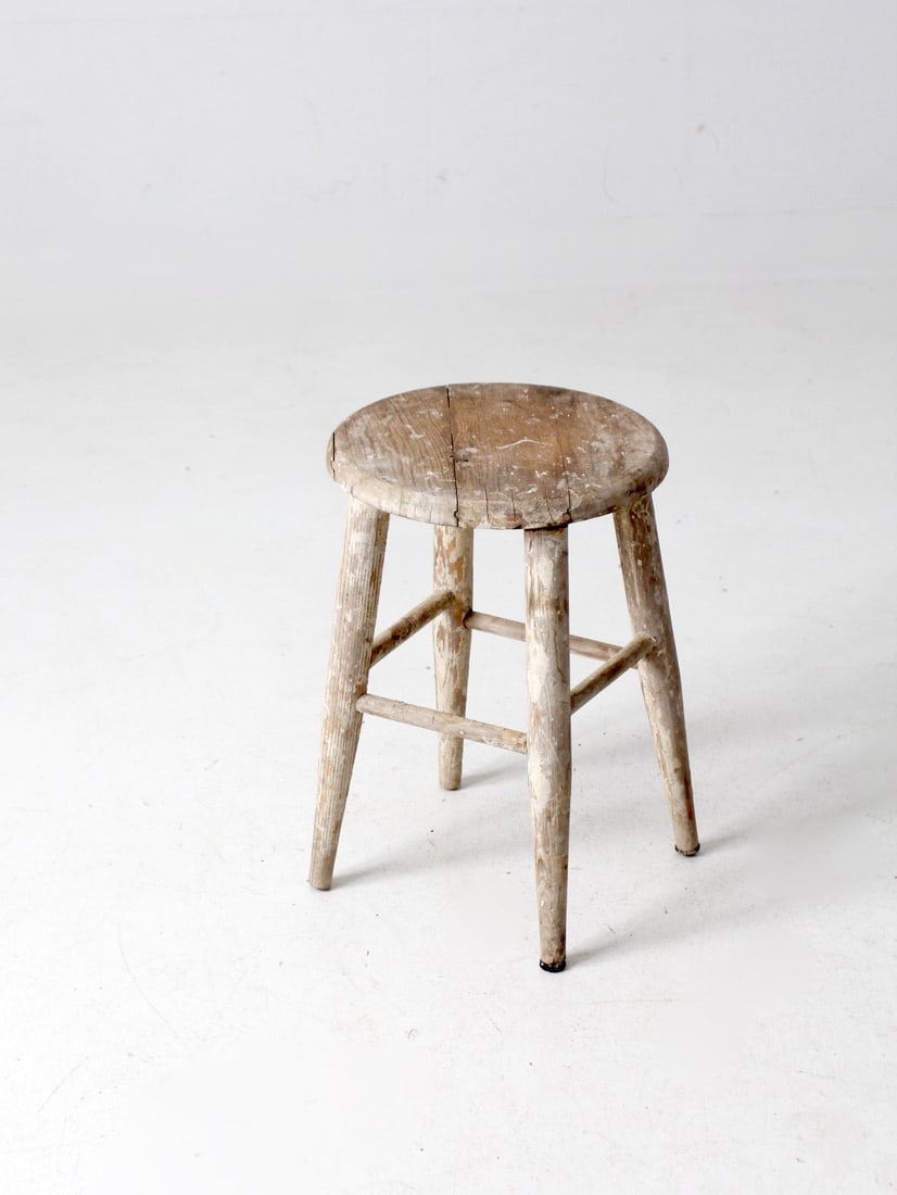 Charming Vintage Wooden Farmhouse Stool with White Paint Remnants: Charming Vintage Wooden Farmhouse Stool with White Paint Remnants This charming vintage farmhouse stool is crafted from wood, showcasing a rustic aesthetic with a round seat and tapered legs. The natu