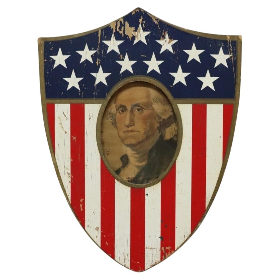 Americana folk art wood shield with 1904 George Washington print: Americana folk art wood shield with 1904 George Washington print Vintage Americana wooden shield frame with a patriotic red and white striped design, a blue field with stars, and a centered oval frame