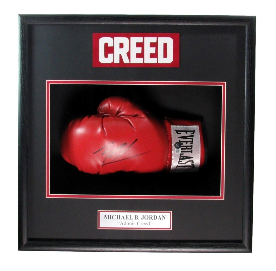 Framed left boxing glove signed by Michael B Jordan Adonis Creed Beckett: Framed left boxing glove signed by Michael B Jordan Adonis Creed Beckett This framed display features a left boxing glove signed by Michael B. Jordan with the inscription "Adonis Creed." The glove is 