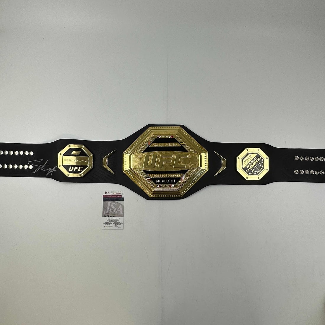 Israel Adesanya Signed UFC Replica Belt with JSA Authentication: Israel Adesanya Signed UFC Replica Belt with JSA Authentication This is a replica UFC Championship belt autographed by Israel "Izzy" Adesanya. The signature has been authenticated by James Spence