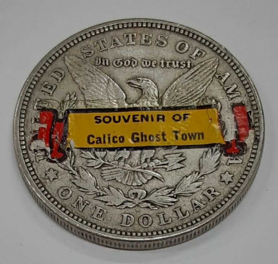 Morgan Dollar 1921-D Silver Calico Ghost Town Souvenir with Reverse Sticker: Morgan Dollar 1921-D Silver Calico Ghost Town Souvenir with Reverse Sticker This 1921-D Morgan Silver Dollar is a circulated coin featuring a sticker on the reverse, serving as a souvenir from Calico 