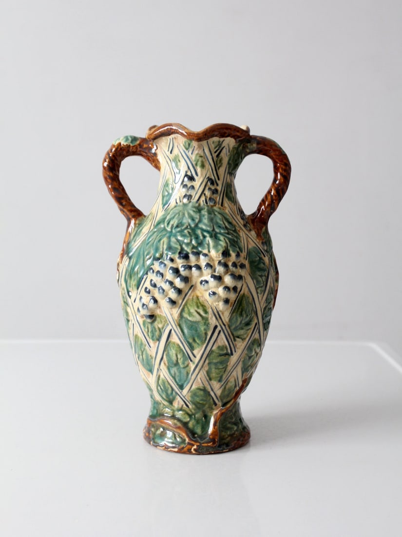 Majolica Urn Vase with Grapevine Relief and Twin Handles: Majolica Urn Vase with Grapevine Relief and Twin Handles This vintage majolica-style vase features sculpted grape clusters and layered leaves set against a lattice background. Designed with twin handl