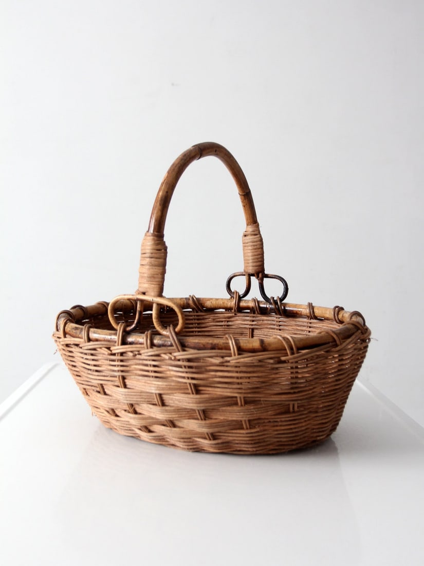 Oval Wicker Basket with Bent Bamboo Handle: Oval Wicker Basket with Bent Bamboo Handle This vintage woven gathering basket features a tightly woven wicker body in warm honey brown tones and an oval form. It is accented by a sculptural bent bamb