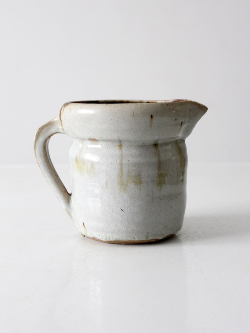 Handmade Vintage Pottery Pitcher Signed 1988 Rustic Charm: Handmade Vintage Pottery Pitcher Signed 1988 Rustic Charm Enhance your dining experience with this charming vintage studio pottery pitcher. Handmade with care, it features a creamy off-white glaze acc