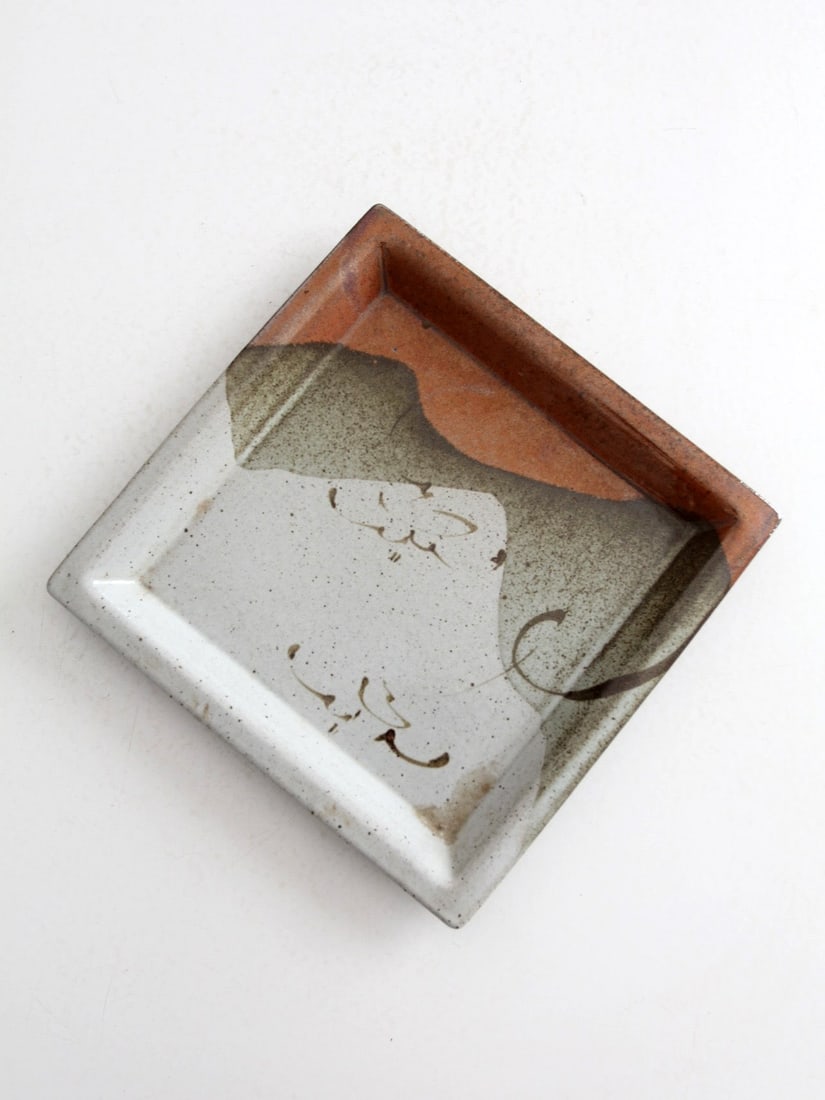Signed square studio pottery plate with lipped edge: Signed square studio pottery plate with lipped edge This vintage studio pottery plate showcases a unique handmade square shape with a lipped edge, signed by the artist. The light gray speckled base is