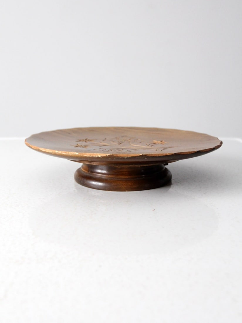 Vintage Folk Art Wood Cake Stand with Carved Floral Detail: Vintage Folk Art Wood Cake Stand with Carved Floral Detail Vintage carved wood cake stand with a low pedestal silhouette, hand-carved floral detailing, a softly irregular edge, and a warm aged finish.