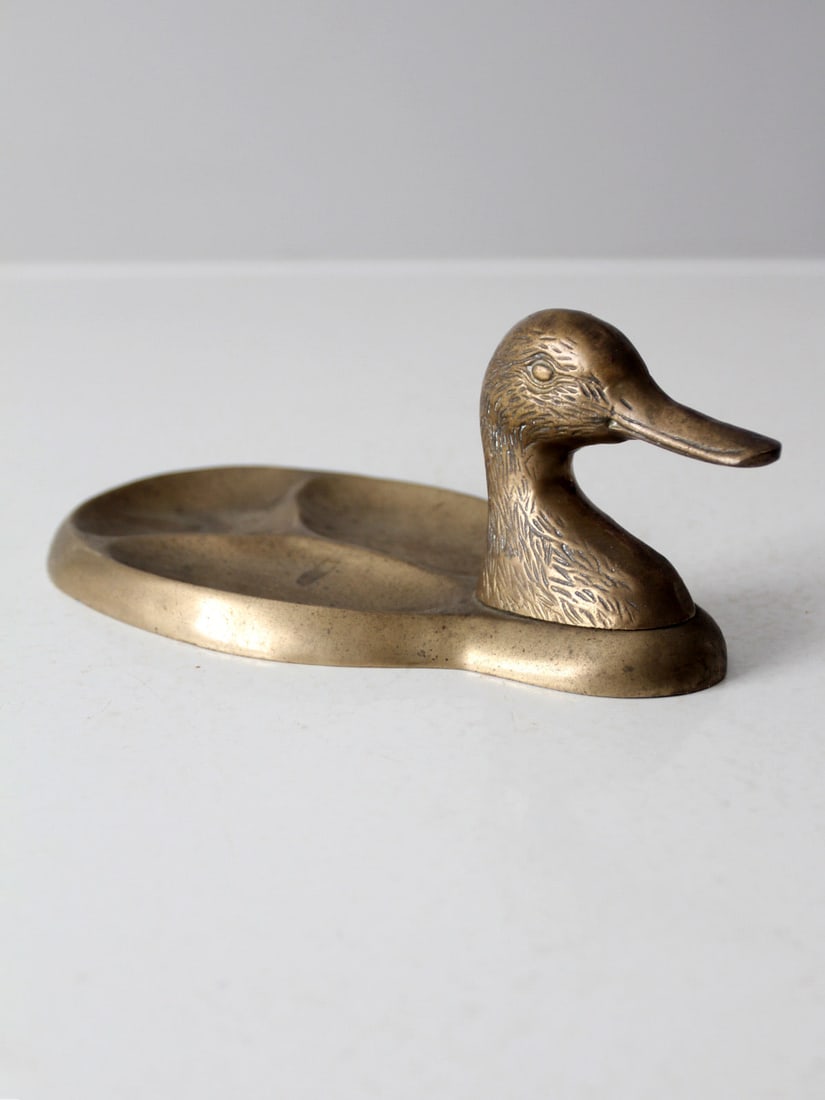 Charming Vintage Brass Duck Valet Tray with Exquisite Detailing: Charming Vintage Brass Duck Valet Tray with Exquisite Detailing Enhance your space with this charming vintage brass duck valet tray. Crafted from solid brass, this valet tray showcases exquisite metal