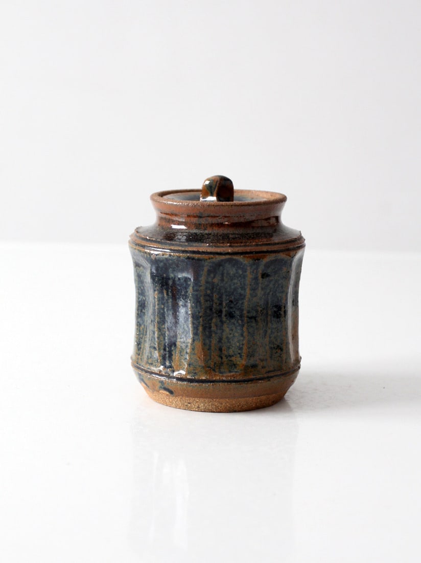 Cylindrical Studio Pottery Lidded Jar in Blue and Brown Glaze: Cylindrical Studio Pottery Lidded Jar in Blue and Brown Glaze This vintage studio pottery jar features a compact, cylindrical silhouette and comes with a fitted lid. The glaze displays a blend of deep