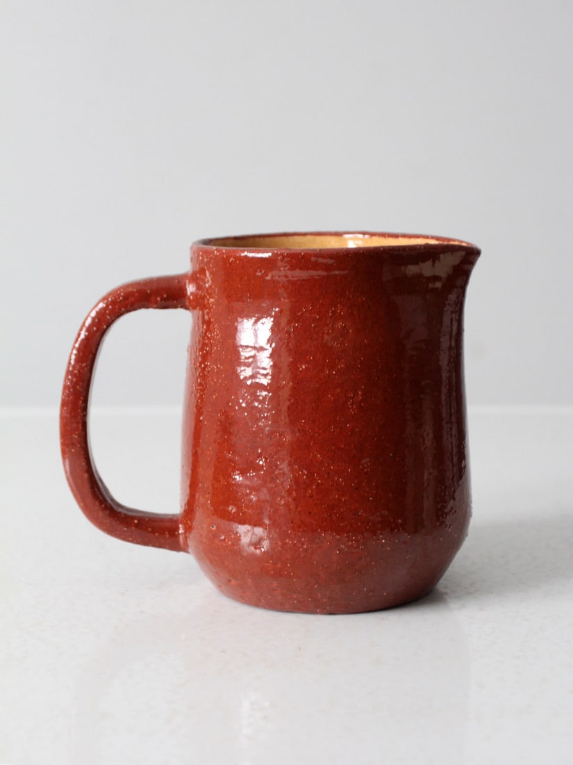 Red Glazed Studio Pottery Pitcher Handmade Vintage 6.25 in: Red Glazed Studio Pottery Pitcher Handmade Vintage 6.25 in This vintage handmade studio pottery pitcher showcases a classic rounded shape complemented by a wide handle and a gently curved spout. The p
