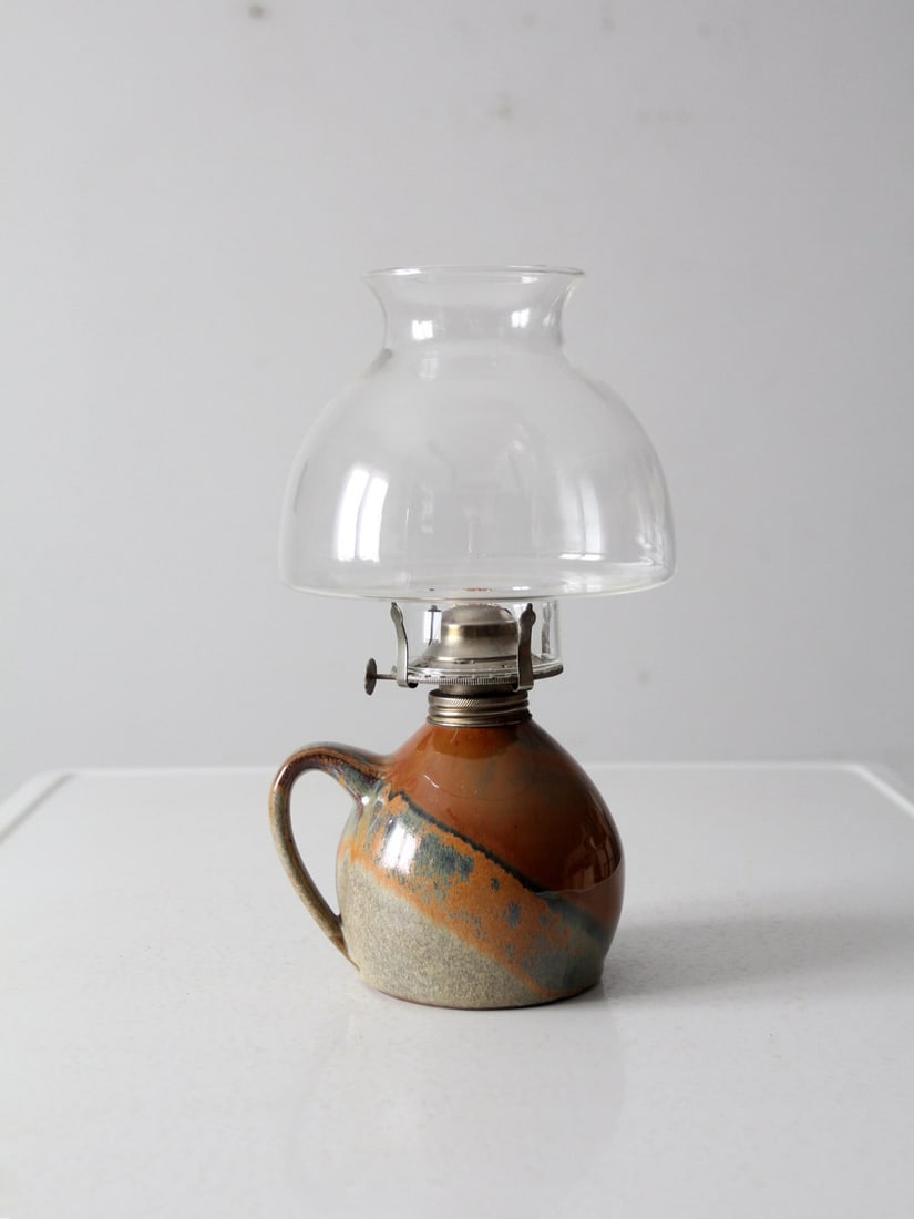 Vintage Handmade Pottery Oil Lamp with Glass Hurricane: Vintage Handmade Pottery Oil Lamp with Glass Hurricane Enhance your living space with this vintage handmade oil lamp that exudes rustic charm. The lamp features a pottery base adorned with a warm brow