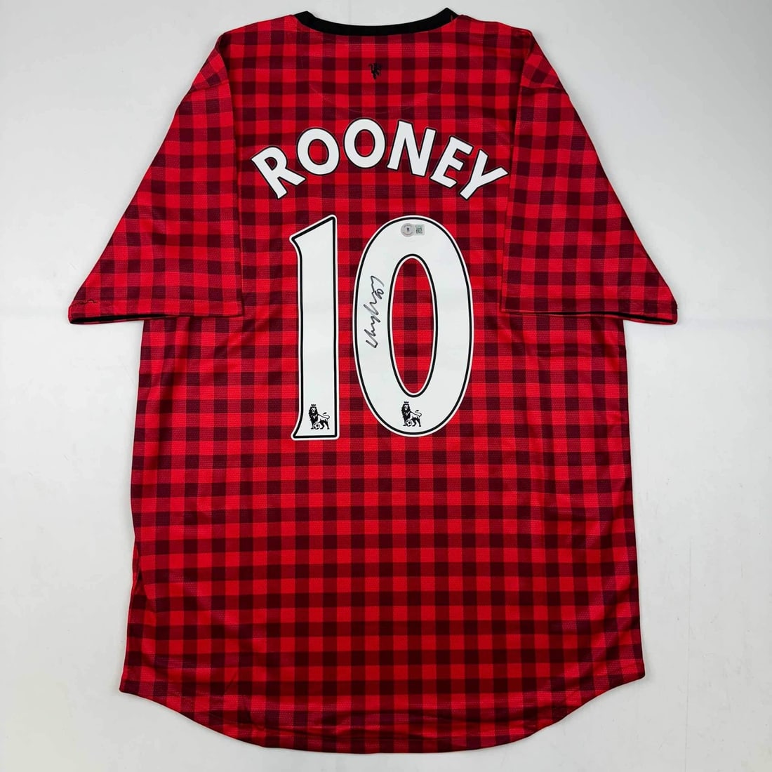 Manchester United red checkered jersey signed by Wayne Rooney Beckett COA: Manchester United red checkered jersey signed by Wayne Rooney Beckett COA Autographed Wayne Rooney Manchester United red checkered jersey. This pre-owned original piece comes with third-party authenti