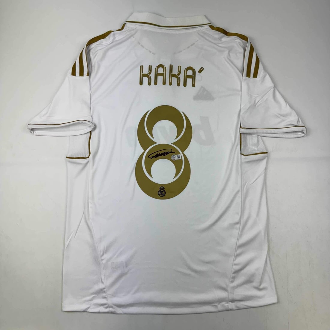 Signed Kaka Real Madrid White Gold Jersey with BAS COA: Signed Kaka Real Madrid White Gold Jersey with BAS COA This original autographed soccer jersey features the legendary Ricardo Kaka, a celebrated player in LaLiga, representing Real Madrid. The jersey 