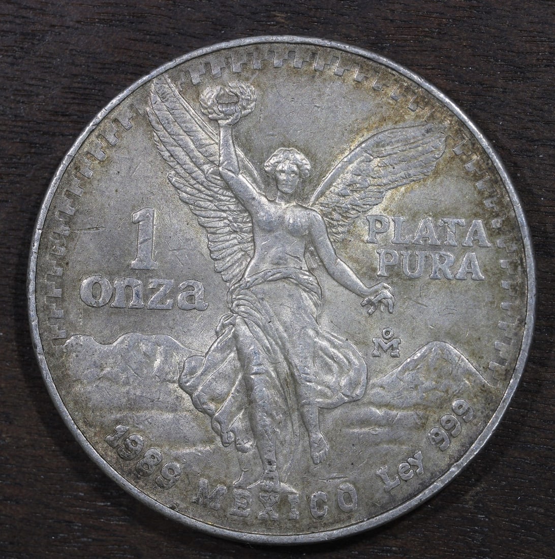 Mexico 1989 Mo Silver Libertad Onza 1 oz .999 Key Date Coin: Mexico 1989 Mo Silver Libertad Onza 1 oz .999 Key Date Coin 1989-Mo Mexico 1 oz Silver Libertad Onza coin with a toned appearance. This key date piece is struck in .999 fine silver and remains uncerti