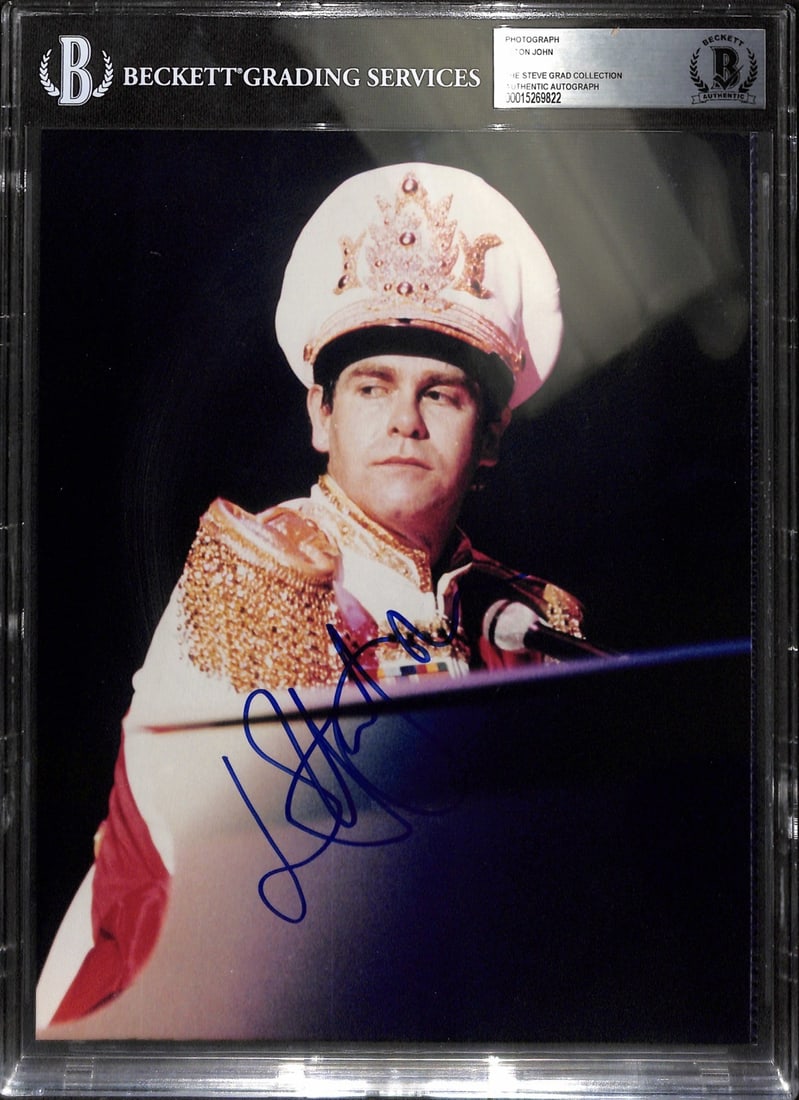 Beckett Authenticated 8x10 Photo Hand Signed by Elton John in Person: Beckett Authenticated 8x10 Photo Hand Signed by Elton John in Person This is an original 8x10 photograph personally signed by Elton John in blue permanent marker. The autograph was obtained in person 