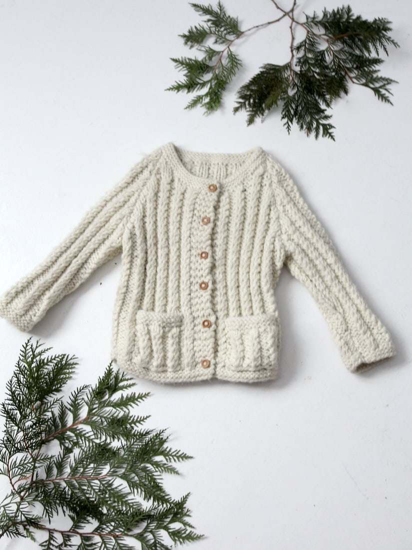 Vintage Hand Knit Children's Cardigan Cream Wool Blend Style: Vintage Hand Knit Children's Cardigan Cream Wool Blend Style This vintage hand-knit children's cardigan is a charming addition to any child's wardrobe. Crafted from a chunky cream knit, it features wo