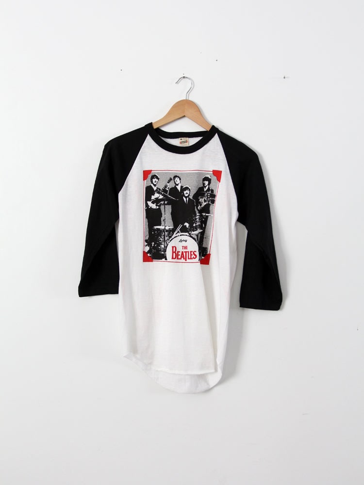 Vintage The Beatles Raglan T-Shirt Classic Design: Vintage The Beatles Raglan T-Shirt Classic Design This vintage The Beatles t-shirt is a must-have for fans and collectors alike. Featuring a classic black and white raglan design, it showcases a timel