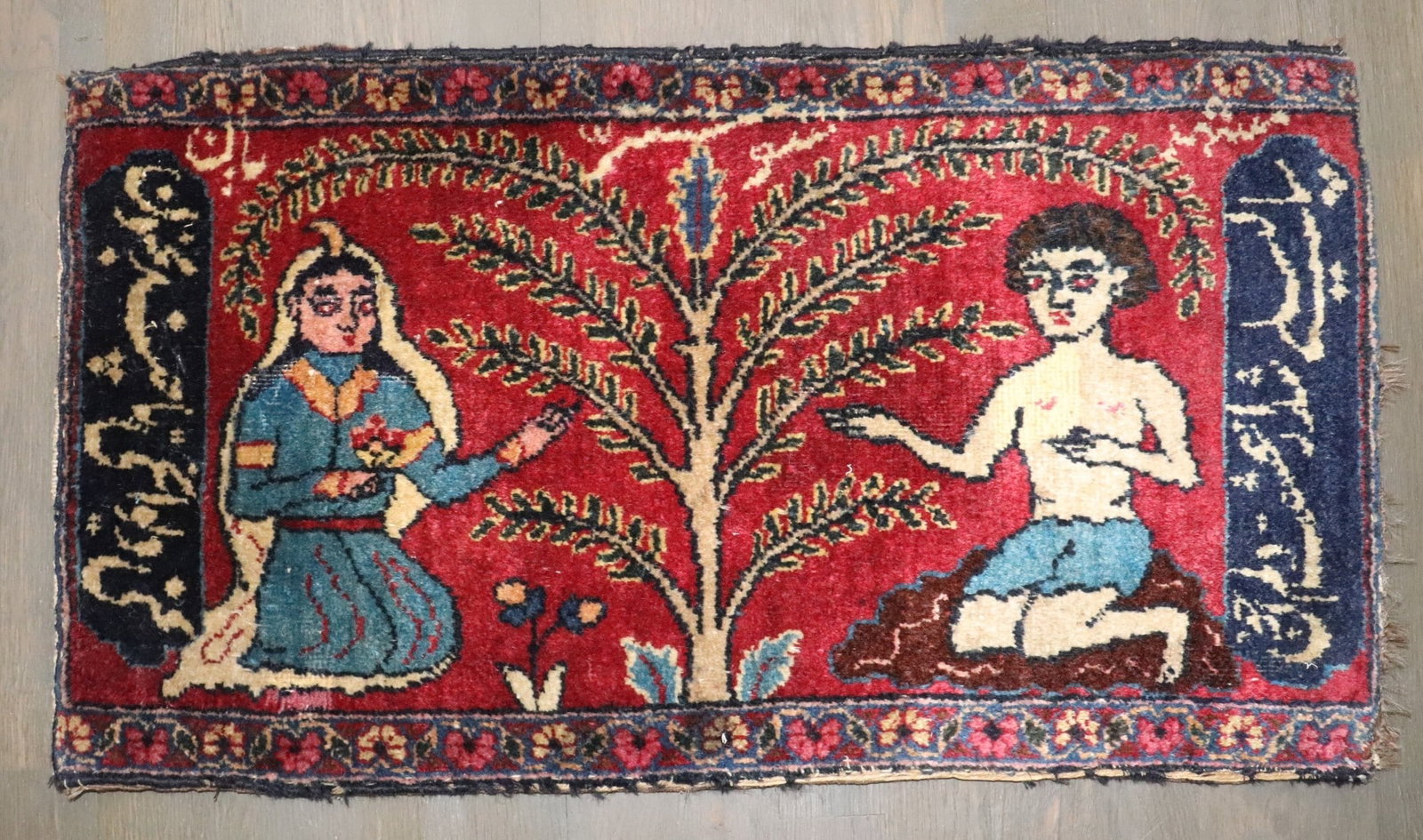 1'4'' x 2'5'' Persian pictorial yastik rug Majnum and Layla: 1'4'' x 2'5'' Persian pictorial yastik rug Majnum and Layla A 19th century Persian pictorial small carpet featuring the Majnum and Layla at the Tree of Knowledge motif. The dark blue side borders incl