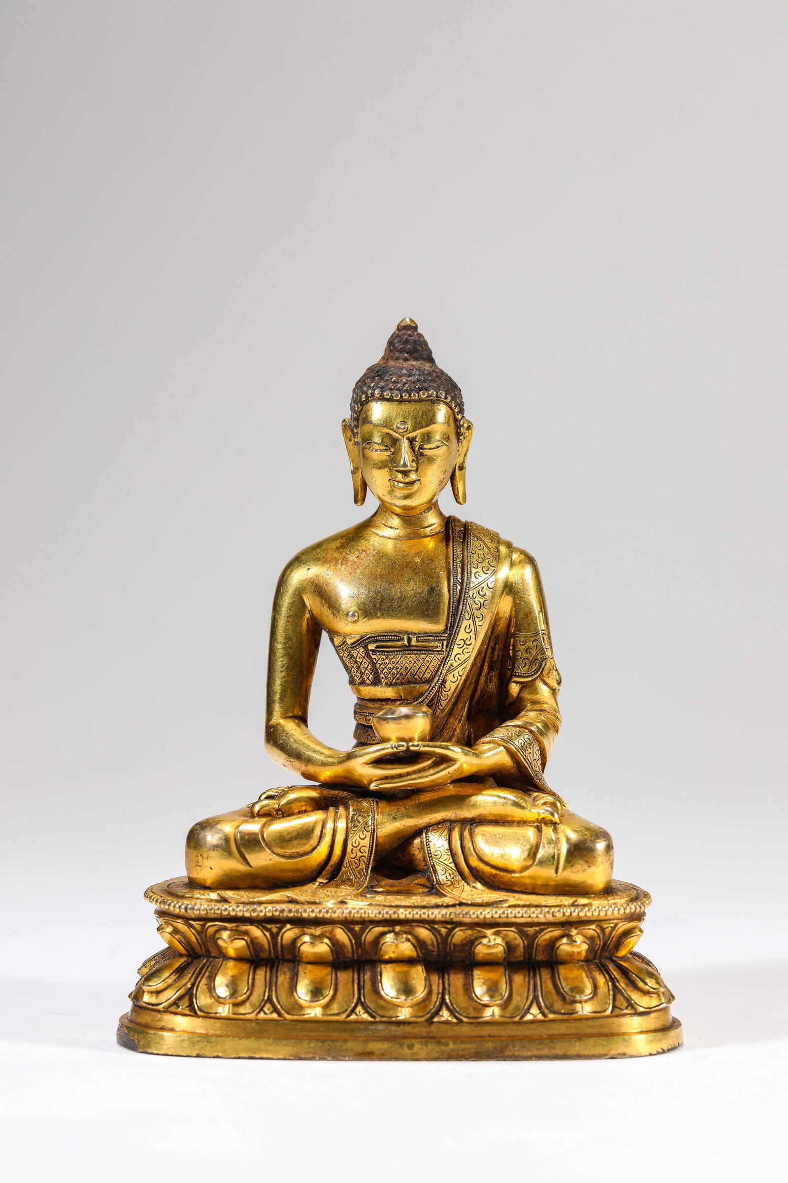 A Gilt-Bronze Figure of Bhaisajyaguru: A GILT-BRONZE FIGURE OF BHAISAJYAGURU Description: Material: Bronze Buddha Weight: 604 g. Length: 9.7 cm x Width: 6.3 cm x Height: 12.5 cm. All measurements are approximate.